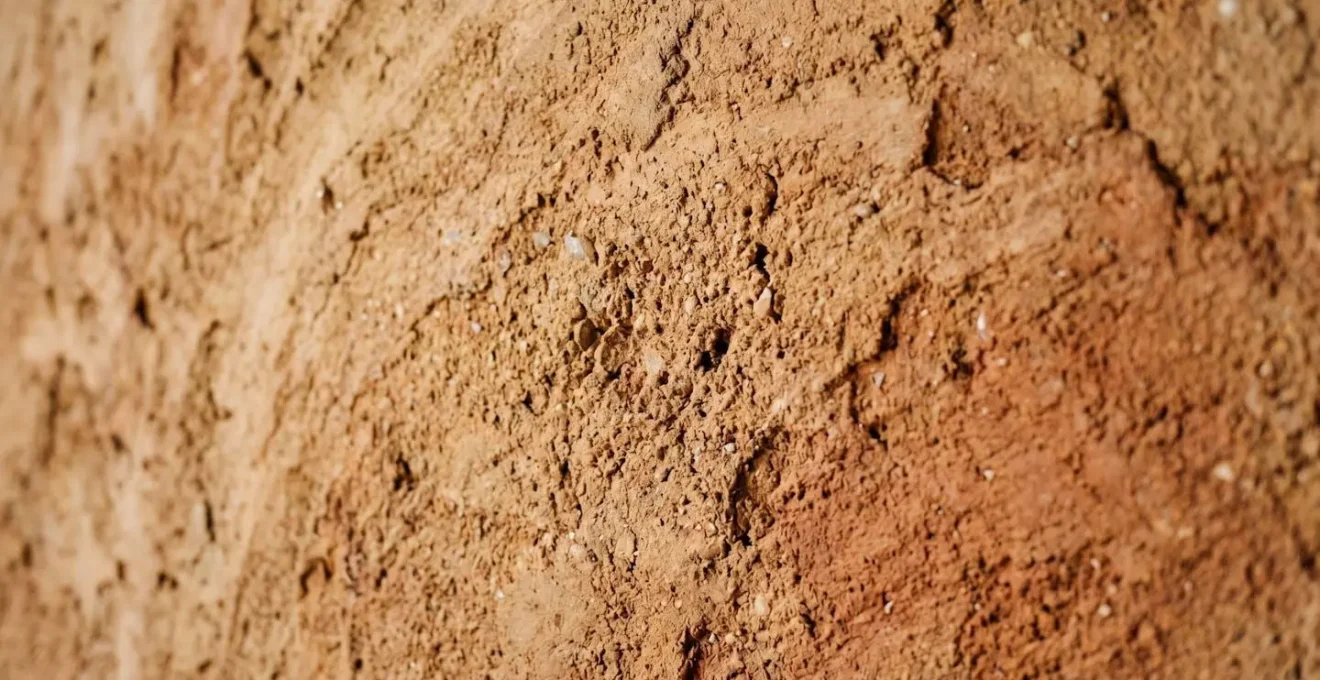 Parete interna con intonaco in terra cruda che mostra texture naturale e gradazioni di colore