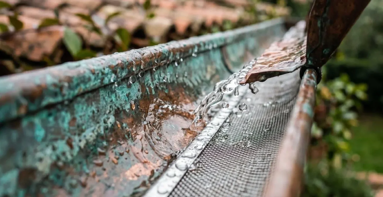 Dettaglio macro di gocce d'acqua piovana che cadono su una grondaia in rame con sistema di filtraggio per cisterna